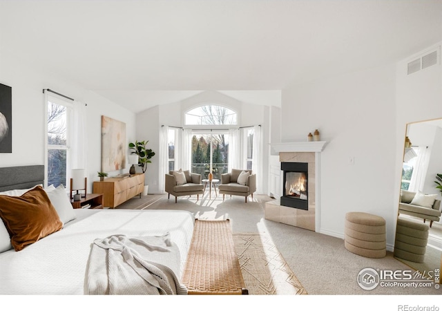 bedroom with a tiled fireplace, vaulted ceiling, visible vents, and light carpet
