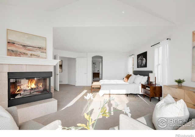 bedroom featuring arched walkways, carpet floors, a fireplace, and lofted ceiling