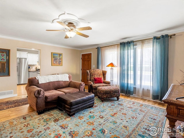 living room with light wood-type flooring, crown molding, ceiling fan, and visible vents