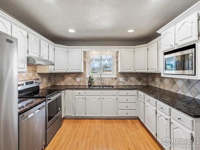 kitchen featuring a sink, white cabinetry, under cabinet range hood, stainless steel appliances, and light wood-style floors