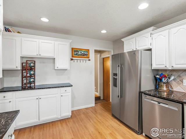 kitchen with tasteful backsplash, light wood-style flooring, dark stone counters, white cabinets, and appliances with stainless steel finishes