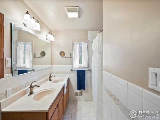 bathroom featuring tile walls, visible vents, a sink, and plenty of natural light