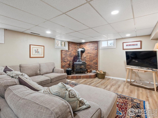 living room with a drop ceiling, wood finished floors, baseboards, and a wood stove