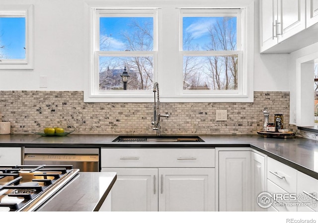 kitchen with white cabinets, dishwashing machine, a sink, and dark countertops