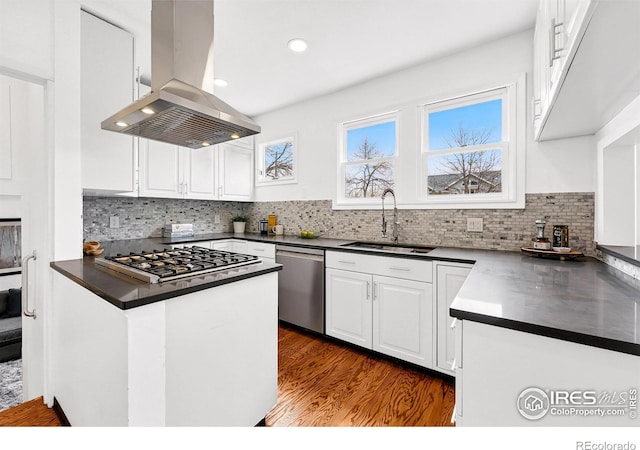 kitchen featuring island exhaust hood, dark countertops, appliances with stainless steel finishes, white cabinetry, and a sink