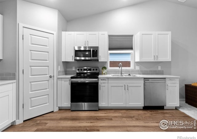 702 S Fulton Ave, Fort Lupton, CO 80621 - kitchen featuring appliances with stainless steel finishes, vaulted ceiling, light wood finished floors, and white cabinetry