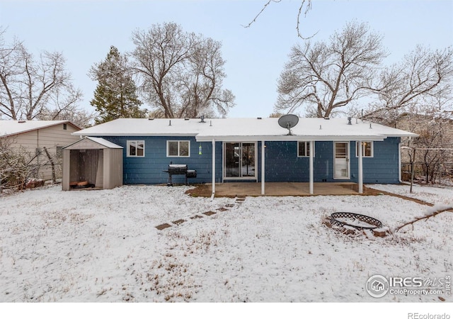 snow covered back of property with an outdoor structure and a storage unit