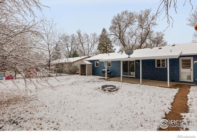 snow covered back of property with an outdoor fire pit and a patio