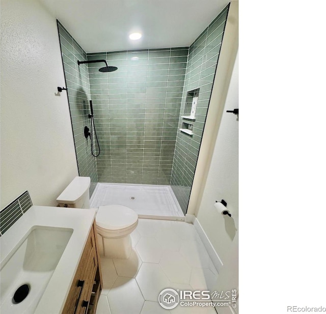 bathroom featuring a tile shower, vanity, toilet, tile patterned floors, and baseboards