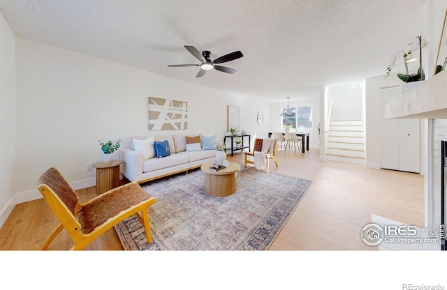 living room with a textured ceiling, light wood finished floors, a ceiling fan, and stairway
