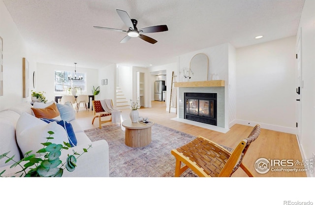 living room featuring ceiling fan with notable chandelier, wood finished floors, baseboards, and a multi sided fireplace