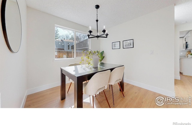dining area with baseboards, light wood-style flooring, a textured ceiling, and an inviting chandelier