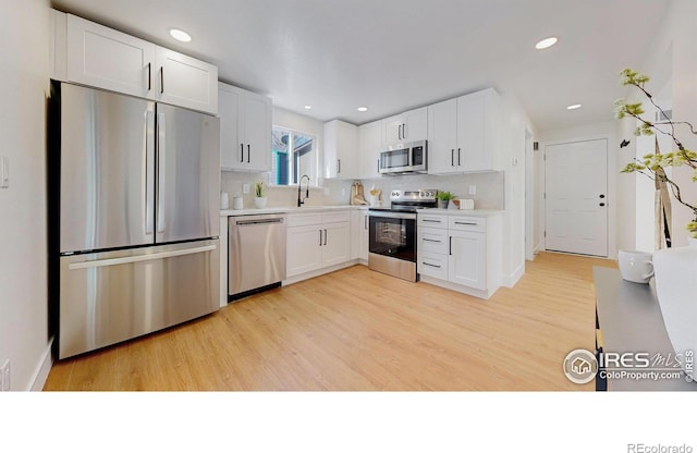 kitchen featuring stainless steel appliances, white cabinets, light wood-type flooring, and backsplash