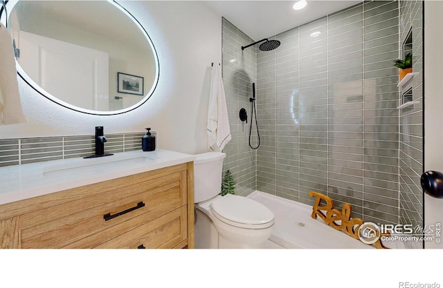 bathroom with toilet, tiled shower, vanity, and recessed lighting