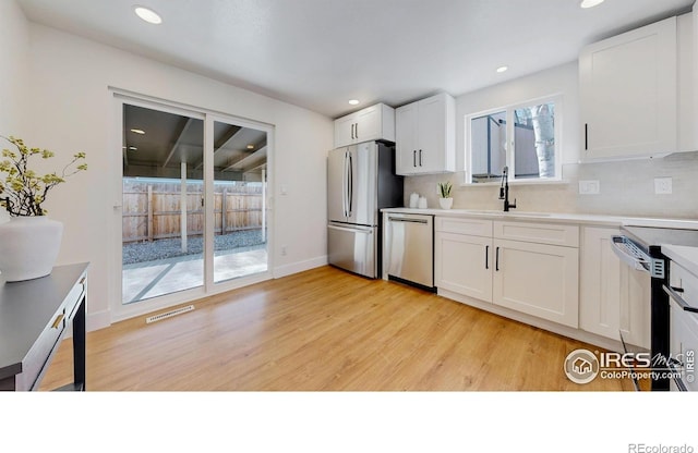 kitchen featuring tasteful backsplash, visible vents, stainless steel appliances, light wood finished floors, and a sink
