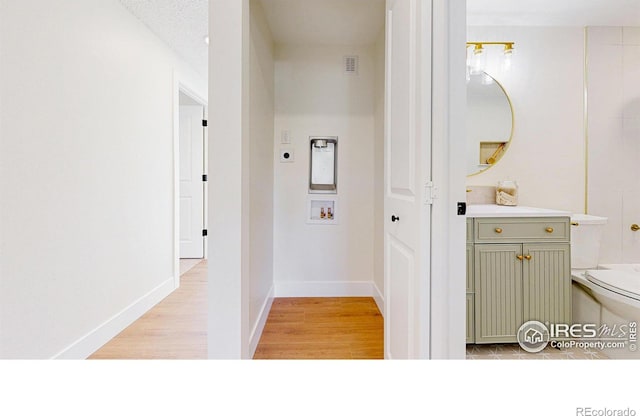 hall with visible vents, baseboards, and light wood-type flooring