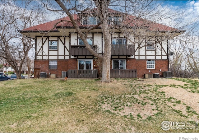 back of house featuring brick siding, central AC, a yard, and stucco siding