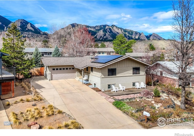 view of front of house with concrete driveway, a mountain view, a garage, fence, and roof mounted solar panels