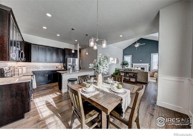 4284 Trapper Lake Dr, Loveland, CO 80538 - dining room with vaulted ceiling, a fireplace, light wood-style flooring, a ceiling fan, and wainscoting