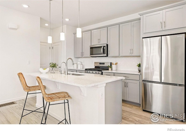 1365 Shale Dr, Erie, CO 80516 - kitchen featuring appliances with stainless steel finishes, a sink, gray cabinets, a center island with sink, and a breakfast bar area