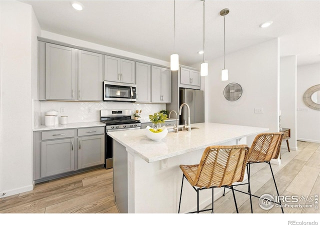 1365 Shale Dr, Erie, CO 80516 - kitchen featuring appliances with stainless steel finishes, gray cabinetry, light wood-style flooring, backsplash, and a breakfast bar area