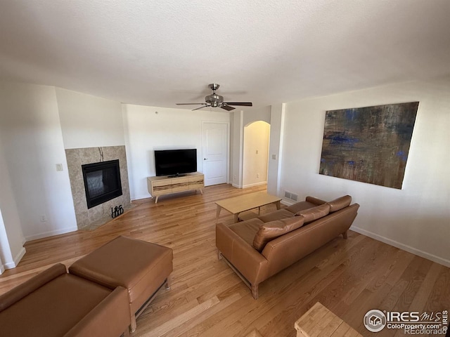 585 Callisto Dr, Loveland, CO 80537 - living room with arched walkways, a ceiling fan, a tiled fireplace, light wood finished floors, and baseboards