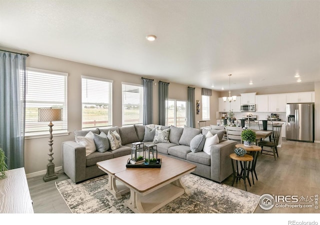 living area with recessed lighting, a notable chandelier, light wood-style floors, and baseboards