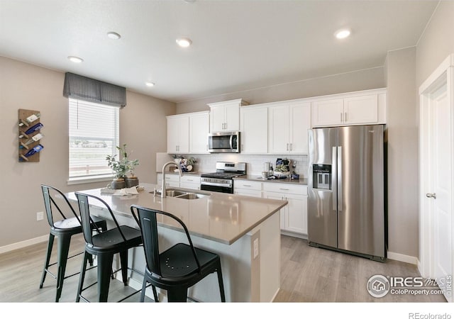 kitchen with a kitchen island with sink, a sink, stainless steel appliances, decorative backsplash, and a breakfast bar area