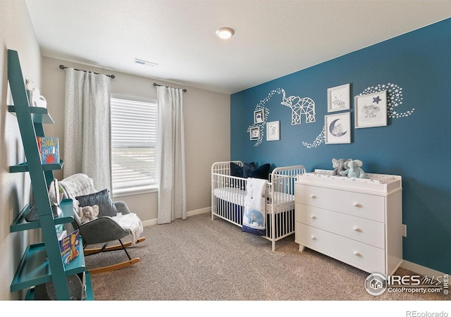 bedroom with visible vents, baseboards, a nursery area, and carpet floors