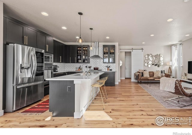 381 Pilsner St, Fort Collins, CO 80524 - kitchen featuring glass insert cabinets, a barn door, a sink, wall chimney range hood, and stainless steel appliances