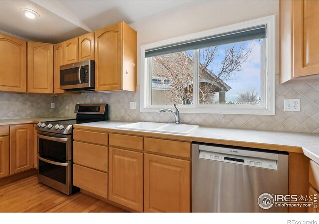 7747 Promontory Dr, Windsor, CO 80528 - kitchen with appliances with stainless steel finishes, a sink, light countertops, light wood-style flooring, and backsplash