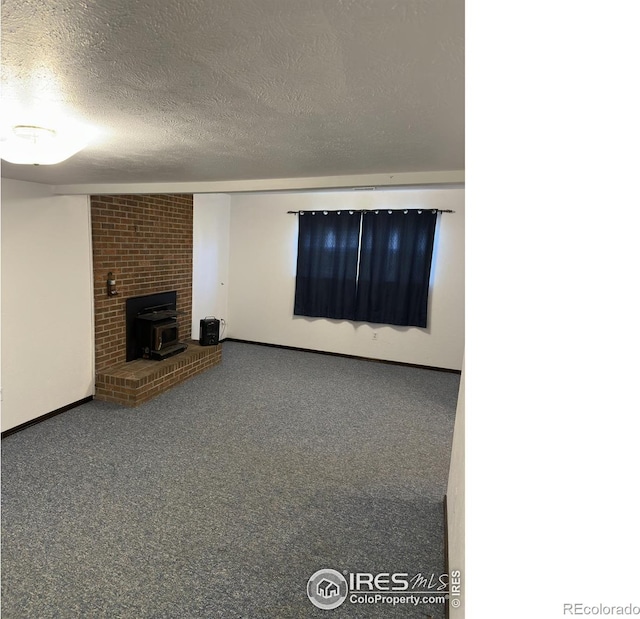 unfurnished living room featuring a wood stove, carpet flooring, baseboards, and a textured ceiling