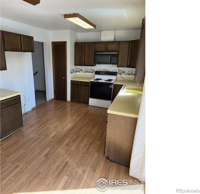 kitchen with black microwave, white electric range, light countertops, and dark brown cabinetry