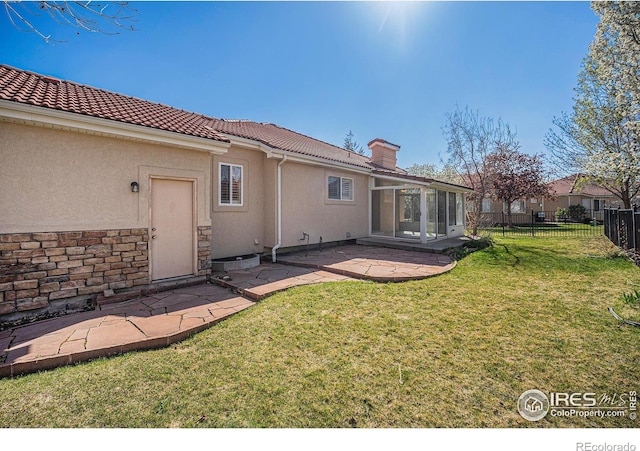 rear view of property featuring a sunroom, a yard, a patio area, fence, and stucco siding