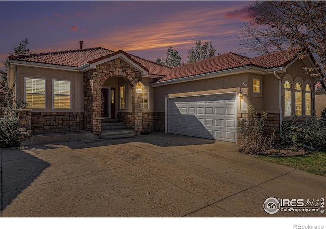 view of front of house with stone siding, a garage, concrete driveway, a tile roof, and stucco siding