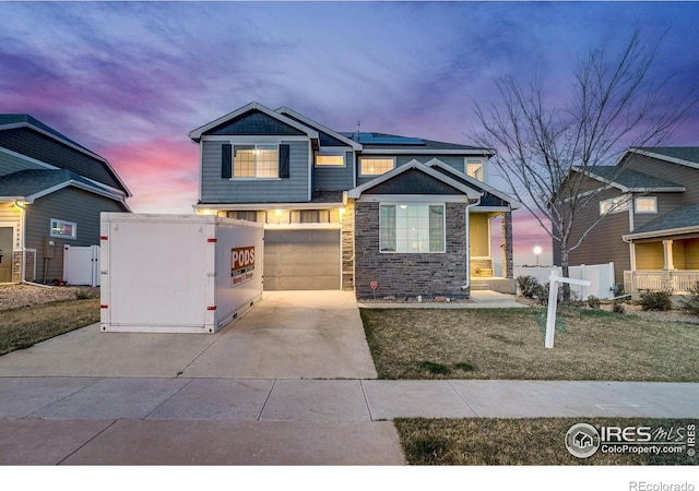 8509 13th St, Greeley, CO 80634 - craftsman-style home featuring concrete driveway, stone siding, an attached garage, fence, and roof mounted solar panels