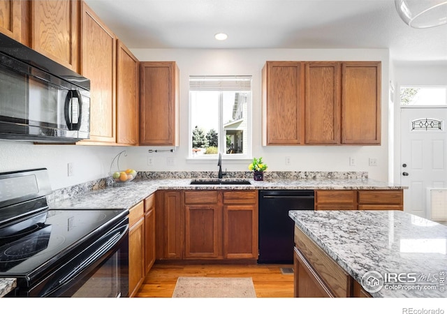 kitchen featuring black appliances, a sink, light wood finished floors, light stone countertops, and recessed lighting