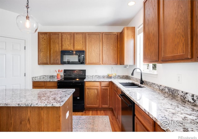 kitchen with black appliances, a sink, brown cabinets, light wood-style flooring, and pendant lighting