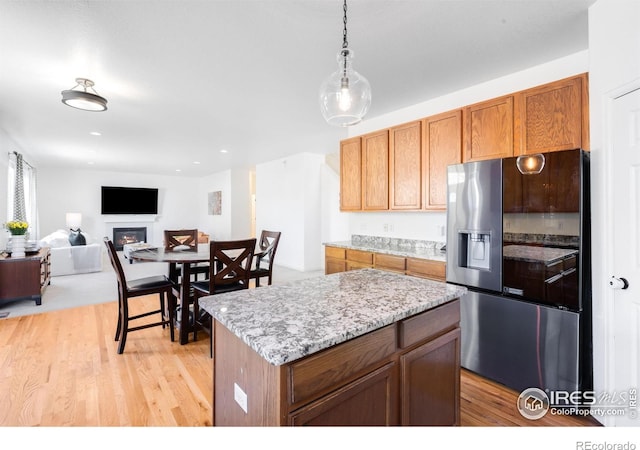 kitchen with stainless steel fridge, light wood-style floors, decorative light fixtures, a warm lit fireplace, and open floor plan
