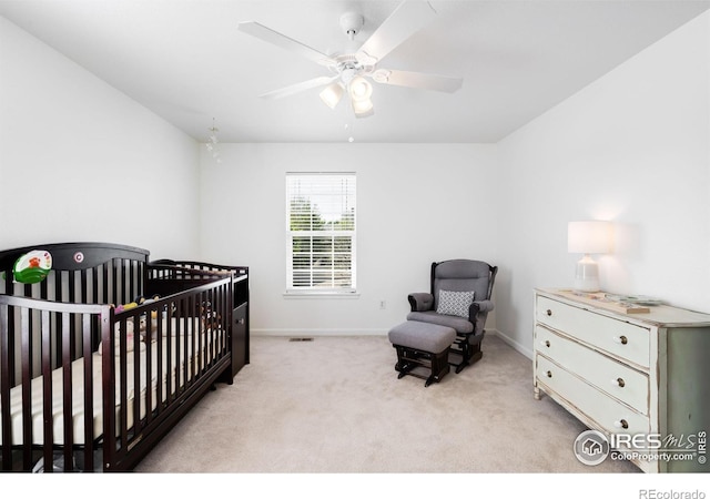 carpeted bedroom featuring a crib, baseboards, and a ceiling fan