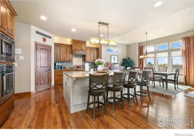 6701 Clovis Ct, Timnath, CO 80547 - kitchen featuring appliances with stainless steel finishes, brown cabinets, an island with sink, recessed lighting, and backsplash