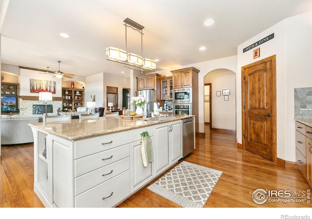 6701 Clovis Ct, Timnath, CO 80547 - kitchen featuring stainless steel appliances, arched walkways, ceiling fan, a sink, and light wood-style floors