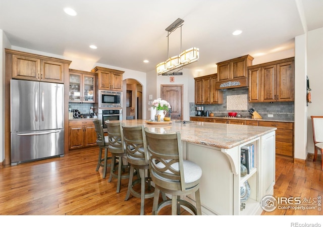 6701 Clovis Ct, Timnath, CO 80547 - kitchen with appliances with stainless steel finishes, brown cabinets, light wood-type flooring, arched walkways, and tasteful backsplash