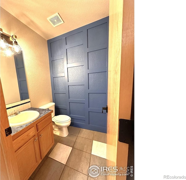 bathroom featuring a textured wall, toilet, tile patterned floors, and vanity