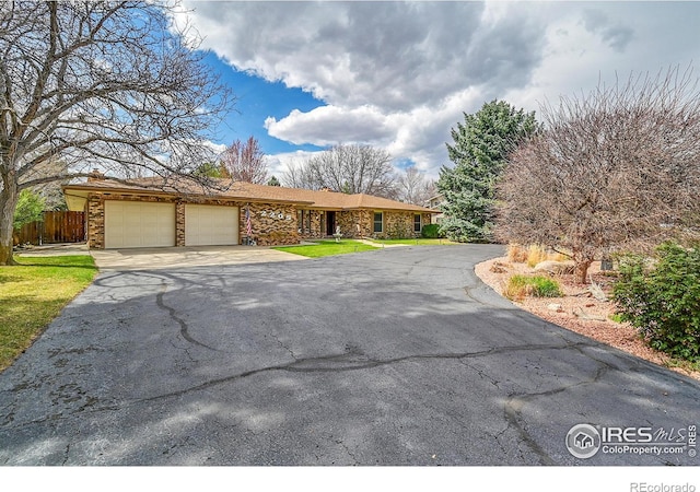 view of front of home featuring stone siding, a garage, fence, and driveway