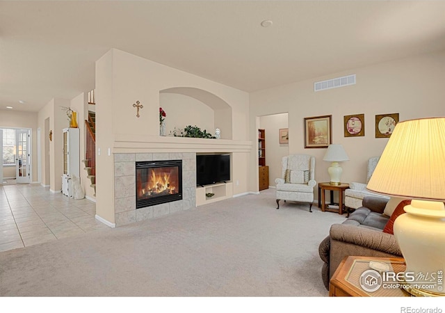 tiled living room featuring a tiled fireplace, carpet flooring, and visible vents