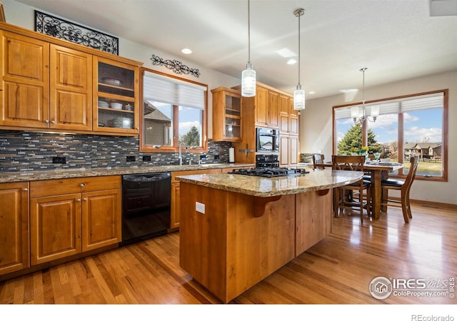 6741 Bandon Dunes Dr, Windsor, CO 80550 - kitchen with a kitchen island, light wood-style floors, brown cabinets, decorative backsplash, and black appliances