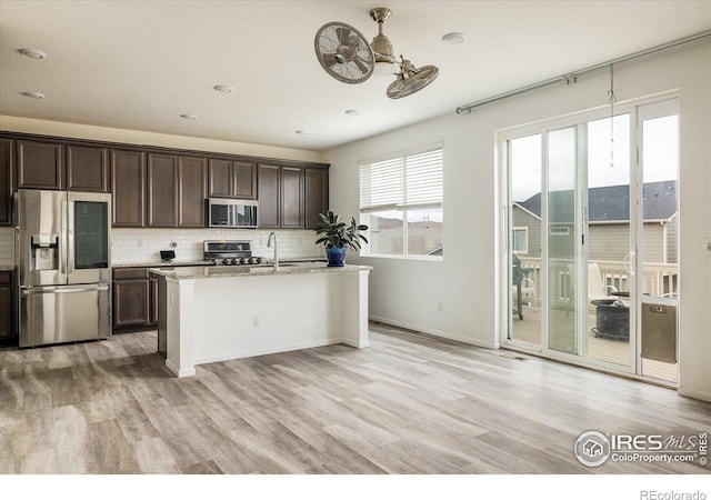 9283 Sedalia St, Commerce City, CO 80022 - kitchen with stainless steel appliances, dark brown cabinetry, light wood-type flooring, and decorative backsplash