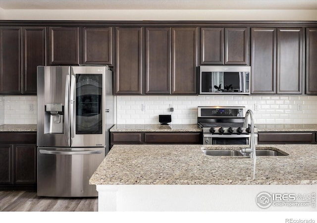 9283 Sedalia St, Commerce City, CO 80022 - kitchen featuring dark brown cabinetry, light stone countertops, appliances with stainless steel finishes, a sink, and wood finished floors