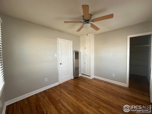 unfurnished bedroom with a spacious closet, dark wood-style flooring, baseboards, and a closet